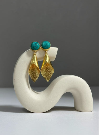 Gold earrings with turquoise stones on a white stand against a gray background